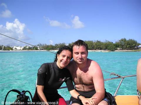 Couple on a boat in turquoise sea, woman in wetsuit, beach behind