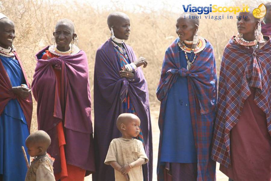 Maasai women wearing beaded jewelry with children, dry bushland