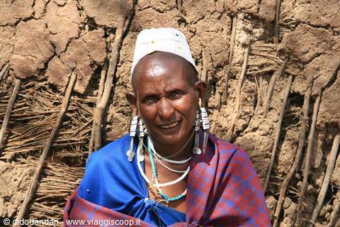 Maasai woman with beaded jewelry and earrings in front of her village