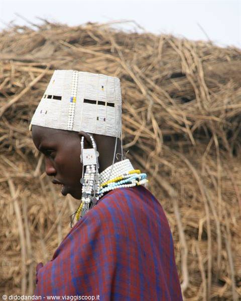 Maasai man wearing white beaded headdress and earrings in front of straw mats