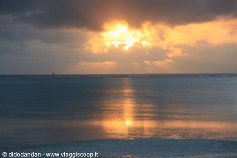 Sun glowing through clouds reflected on calm sea, distant sail