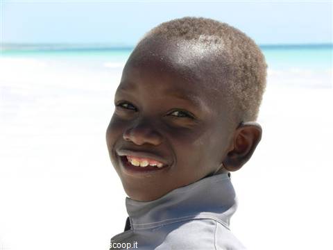 Smiling boy on white sand beach, turquoise sea behind him