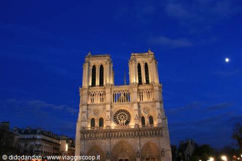 Notre-Dame facade lit up at night under blue sky with moon