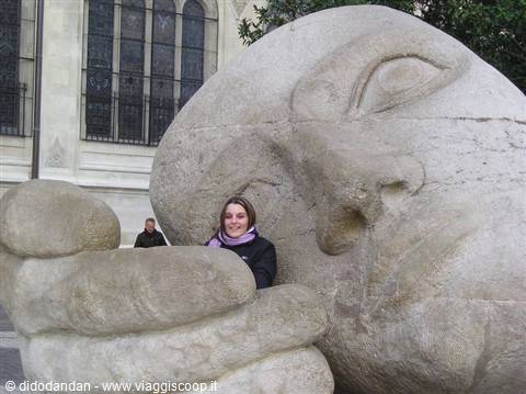 Tourist beneath a carved stone head and hand sculpture in Zurich