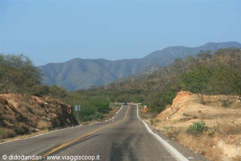 Empty paved road with yellow lines crossing dry hills and mountains