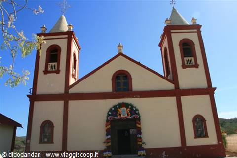 White and red church with twin towers, blue sky, flower-decorated entrance