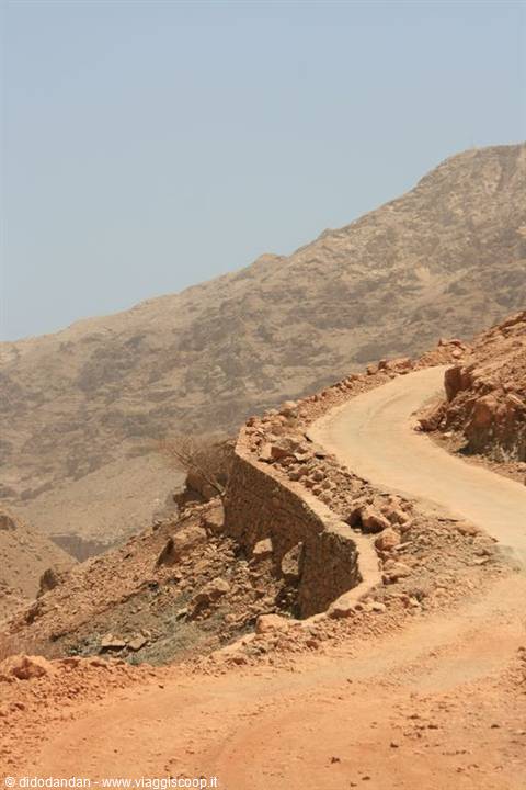 Winding dirt road through arid rocky mountains under a blue sky