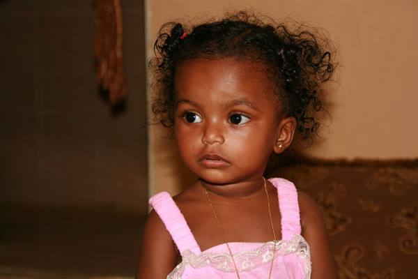 Toddler girl with curly hair, earrings, pink dress, warm indoor light