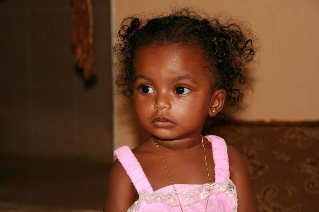 Toddler girl with curly hair, earrings, pink dress, warm indoor light