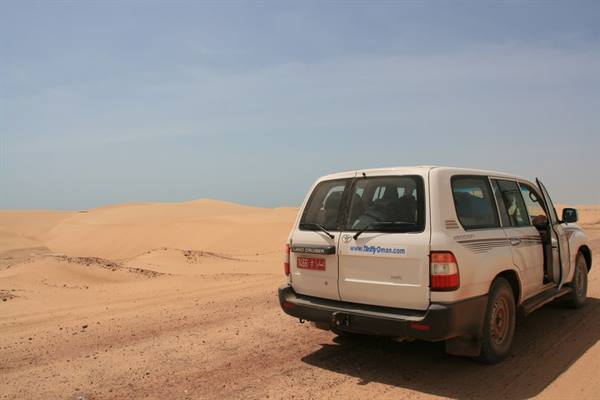 White Toyota 4x4 parked between sand dunes under a clear blue sky