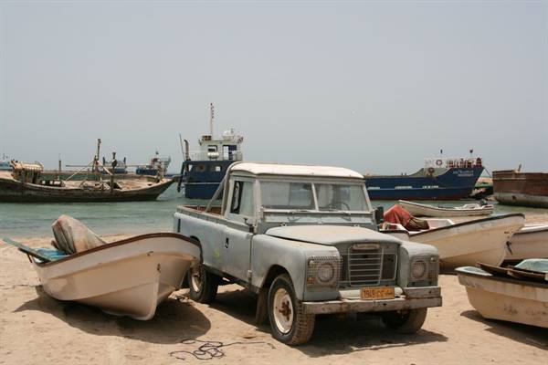 Old Land Rover parked among wooden fishing boats on a sandy beach
