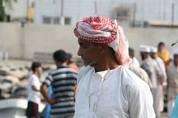 Man wearing red checkered turban and white robe among crowd at market