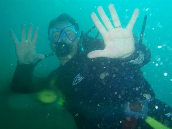 Scuba diver in mask and tank waves both hands in green water
