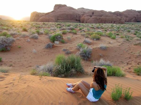 Woman with camera sitting on red sand dunes in Monument Valley