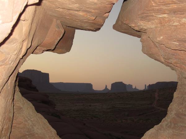 Monument Valley seen from inside a reddish rock cave at dusk