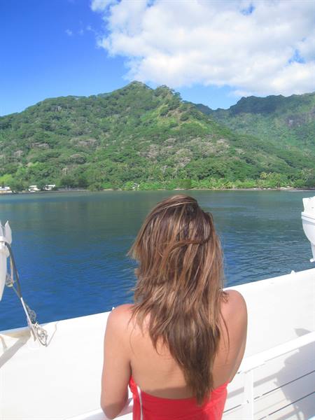Woman in red top on white boat facing green mountains and blue bay