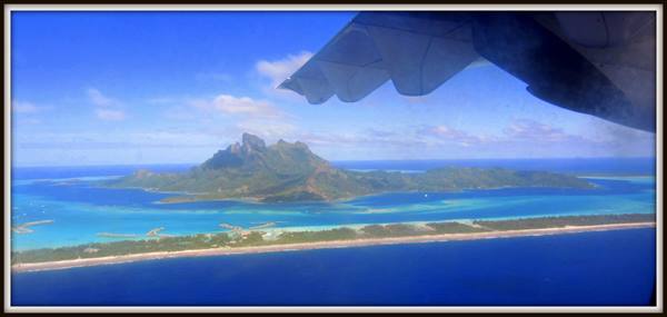 Plane wing over the turquoise lagoon and volcanic peaks of Bora Bora
