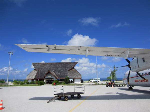 Air Tahiti plane on tarmac, luggage cart, thatched-roof terminal building