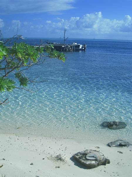 Clear turquoise water over sandy beach, boat moored at wooden jetty