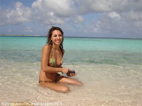 Woman in bikini kneeling in turquoise water, holding a camera