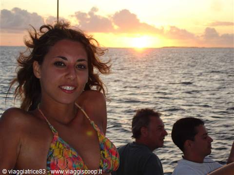 Smiling woman in colorful bikini on a boat, open sea, low sun among clouds