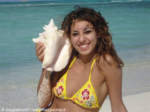 Girl in yellow bikini smiles holding a large conch shell on the beach