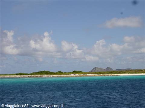 Turquoise sea and white beach with arid hills under white clouds