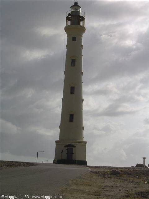 California Lighthouse in Aruba, white tower against cloudy sky, dirt road