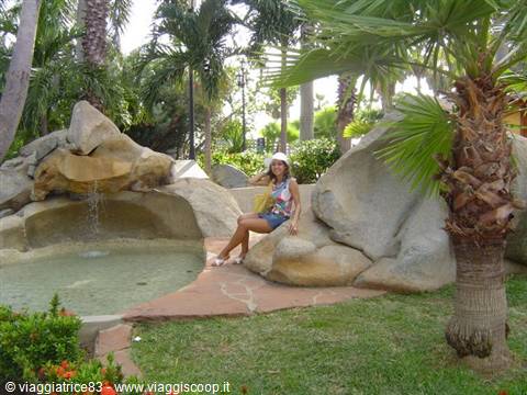 Woman sitting on a large rock beside a small waterfall among palm trees