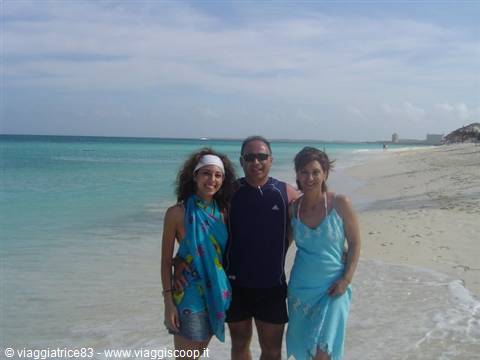 Three people smiling and hugging on white sand beach with turquoise sea