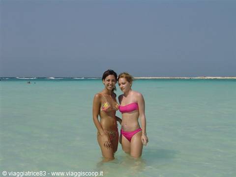 Two women in bikinis wading in turquoise sea water on a tropical beach