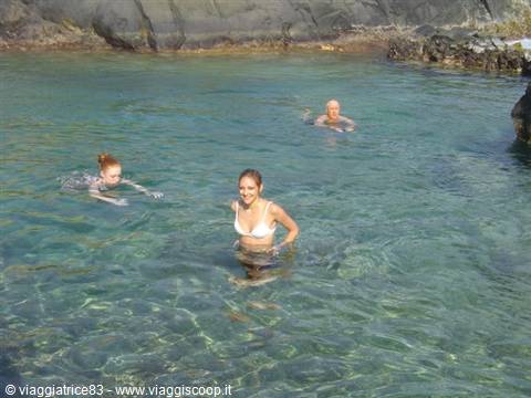 Swimmers enjoying clear turquoise water among dark volcanic rocks