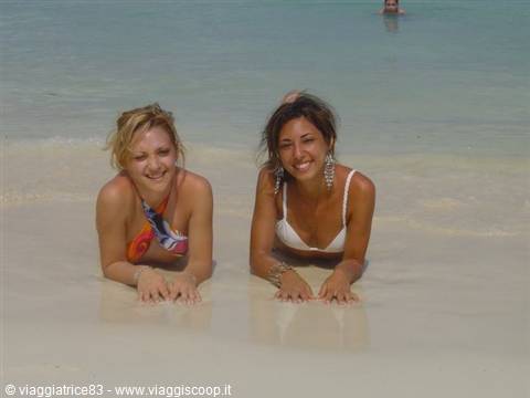 Two girls lying on wet sand, laughing in bikinis by the sea