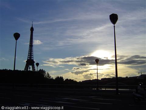 Eiffel Tower silhouetted at dusk among street lamps and clouds