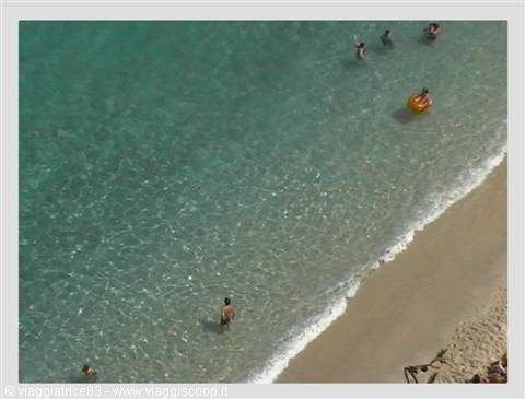 Swimmers in clear turquoise water beside the golden sand beach