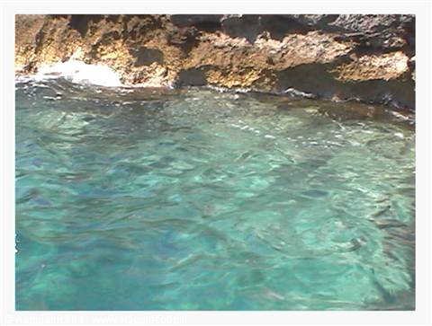 Clear turquoise water against dark volcanic rocks lit by sunlight