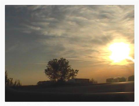 Low sun behind clouds, tree and houses silhouetted from the road