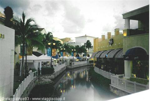Water canal between palm trees and shops with awnings, cloudy sky