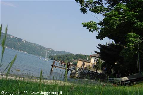 Hull and pier on the lake, yellow house among trees, boat on green grass