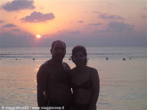 Couple in swimwear by the sea under a pink and orange sky