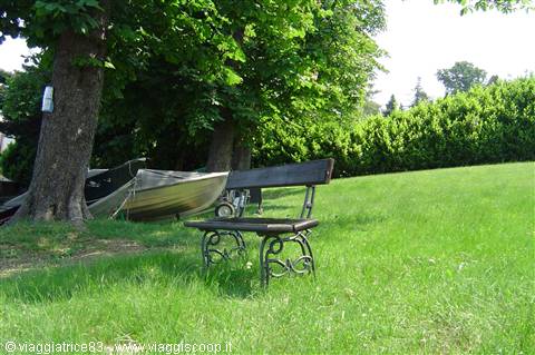 Wrought iron bench on green grass, covered boat beneath large trees