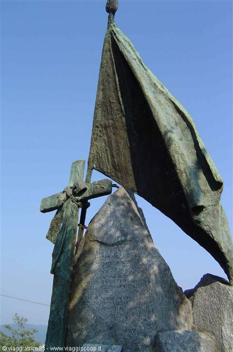 Bronze monument with flag and cross on stone boulder, blue sky