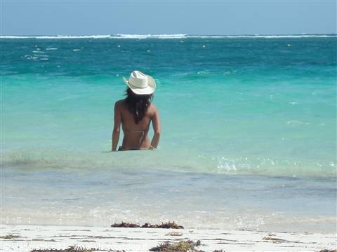 Woman in straw hat and bikini standing in turquoise water by the sandy beach