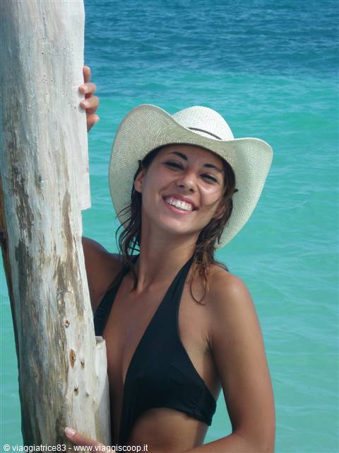 Woman in straw hat and black bikini beside bleached wooden trunk, turquoise sea