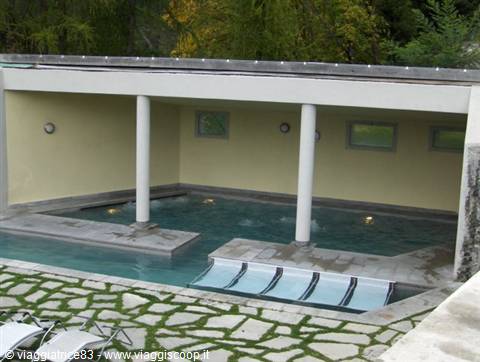 Covered thermal pool with white columns and loungers on stone pavement