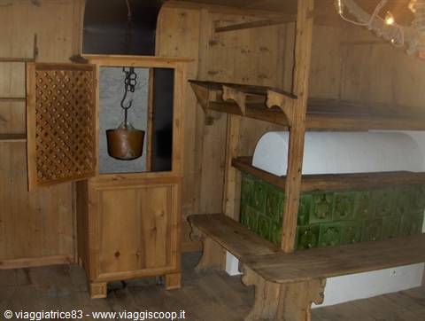 Green tiled stove and wooden cupboard with hanging copper pot in museum room