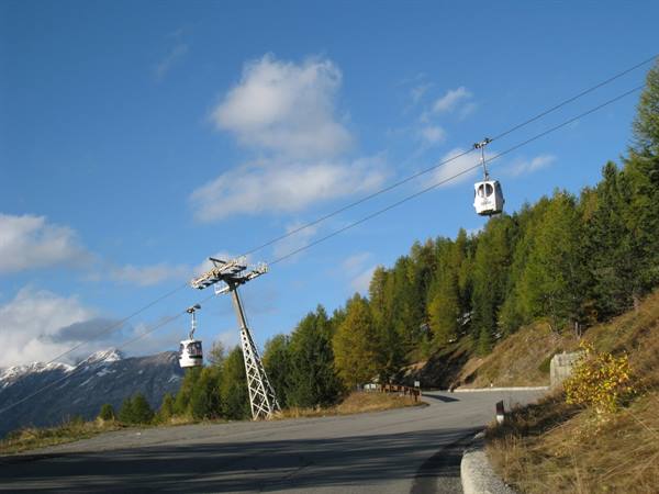 White cable car above a mountain road, firs and steel pylon