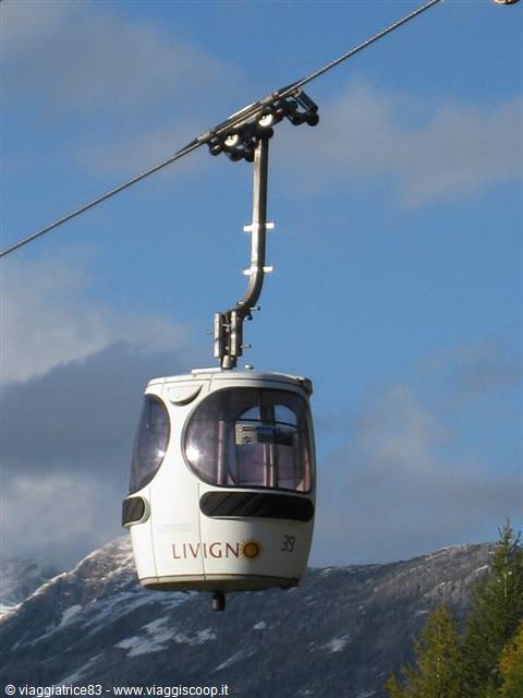 Livigno cable car cabin hanging on the wire, snowy mountains and blue sky