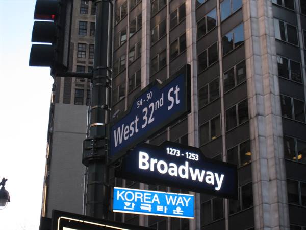 Street signs for Broadway and West 32nd St in front of skyscraper