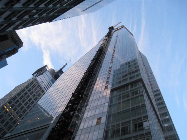 Glass skyscraper under construction with crane, seen from below between buildings